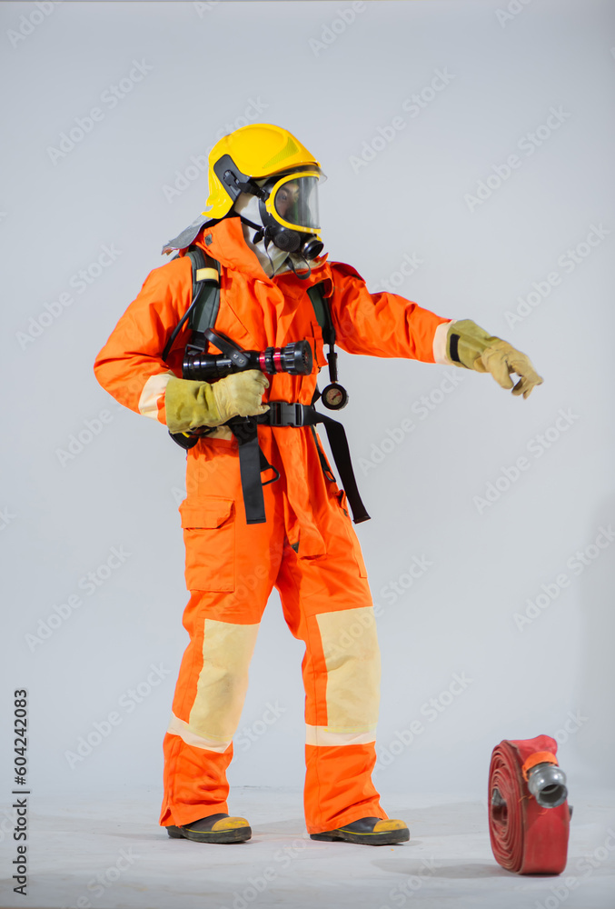 Vertical picture shows a firefighter standing and holding a fire hose while pointing his finger and looking sideways on a white background. Vertical picture shows a firefighter standing and holding a fire hose while pointing his finger and looking sideways on a white background.