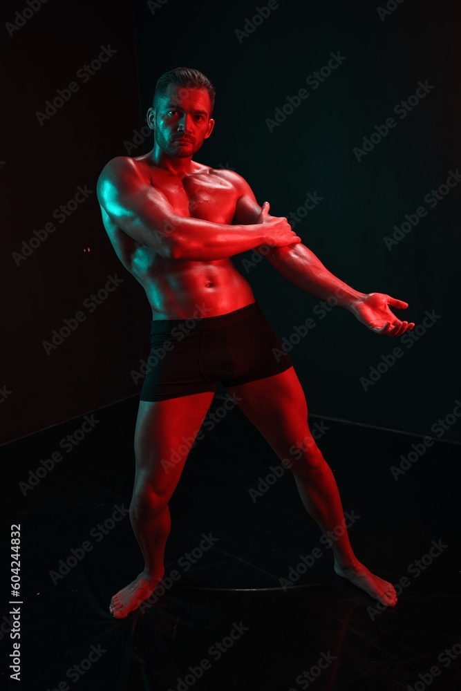 Man bodybuilder posing muscles with nude fitness torso, isolated on black background in neon light. Advertising, sports, active lifestyle, colored light, competition, challenge concept. 