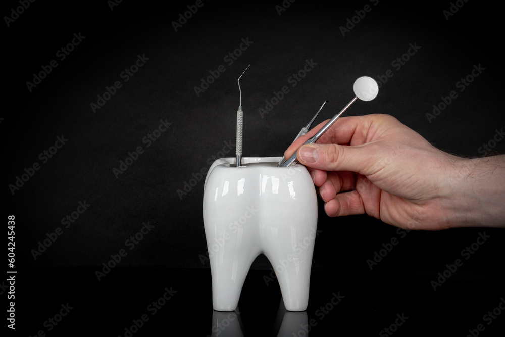 White ceramic tooth cup and dental equipment, dental mirror and dental probe and a man hand on black reflective background.
