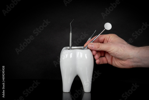 Obraz na płótnie White ceramic tooth cup and dental equipment, dental mirror and dental probe and a man hand on black reflective background. w salonie