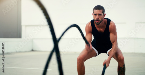 Man, fitness and battle ropes in training, exercise or workout for physical wellness outdoors. Fit, active and serious male person exercising with rope for intense body endurance, stamina or cardio