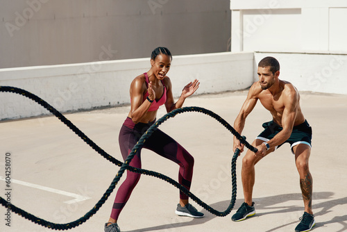 Woman, personal trainer and battle rope for workout, exercise or training in fitness outdoors. Fit, active or serious coaching with man person exercising with ropes for sports endurance or motivation © Emil L/peopleimages.com