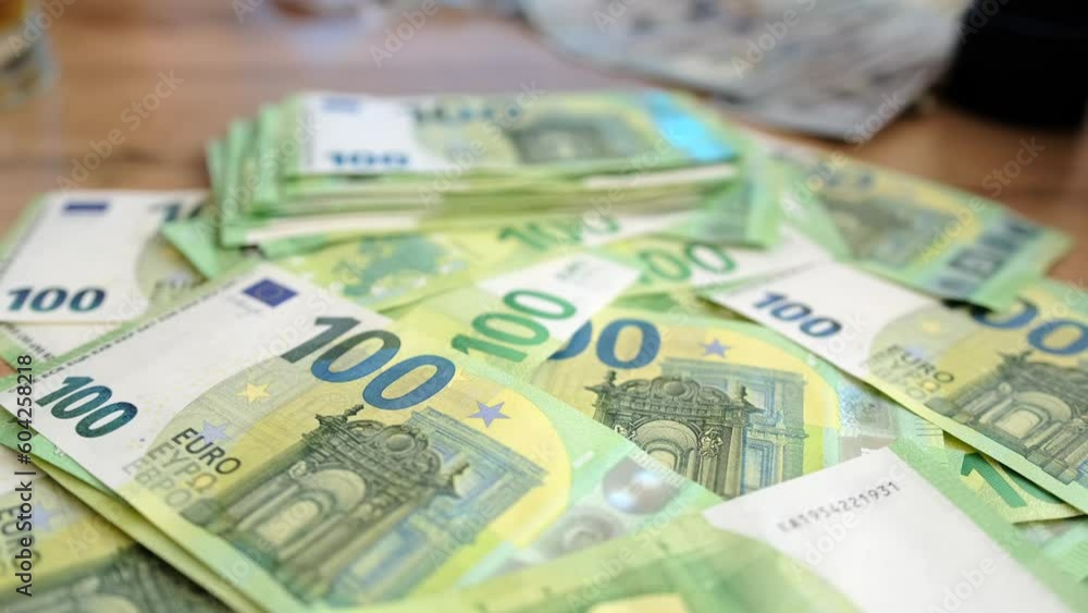 Slow motion close-up over a pile of hundred euro banknotes that lie on a wooden table. Many 100 euro bills. Financial management and budgeting. Slow motion close-up over a pile of hundred euro banknotes that lie on a wooden table. Many 100 euro bills. Financial management and budgeting.
