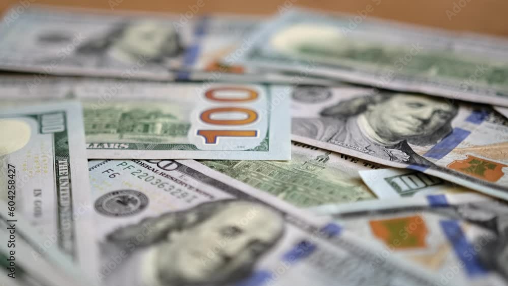 Slow motion close-up over a pile of hundred dollar banknotes that lie on a wooden table. Many 100 dollar bills cash. Financial management and budgeting. Slow motion close-up over a pile of hundred dollar banknotes that lie on a wooden table. Many 100 dollar bills cash. Financial management and budgeting.
