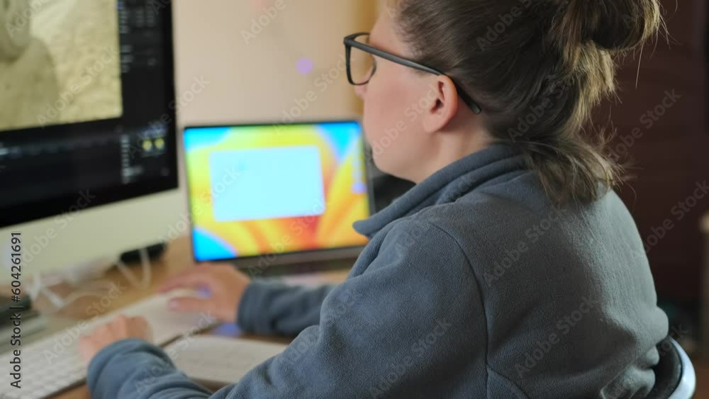 Woman sitting at desk in front of computer monitor and laptop is watching video with car moving, with a cup of coffee on the table. Working at home. Woman sitting at desk in front of computer monitor and laptop is watching video with car moving, with a cup of coffee on the table. Working at home.