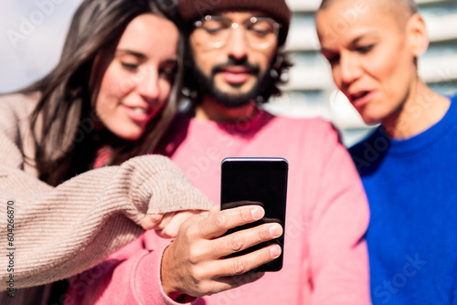 man holding a mobile phone sharing a moment with two female friends, focus on the phone, concept of technology of communication and connectivity in a digital world