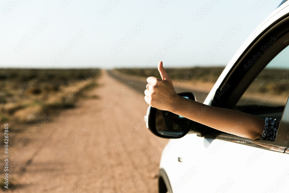 Happy woman traveler showing thumb up out of car window, enjoys road trip in a car during summer holidays in Australia Happy woman traveler showing thumb up out of car window, enjoys road trip in a car during summer holidays in Australia