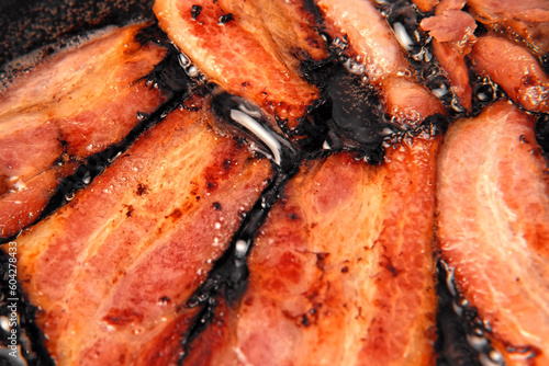 Frying Bacon Slices in a Pan. Crispy Pieces of Delicious Red Thin Smokey Bacon Fried in a Hot Skillet. Traditional Breakfast. Smoked Bacon Rasher or Strip Being Cooked. Grill. Fat High Calorie Food