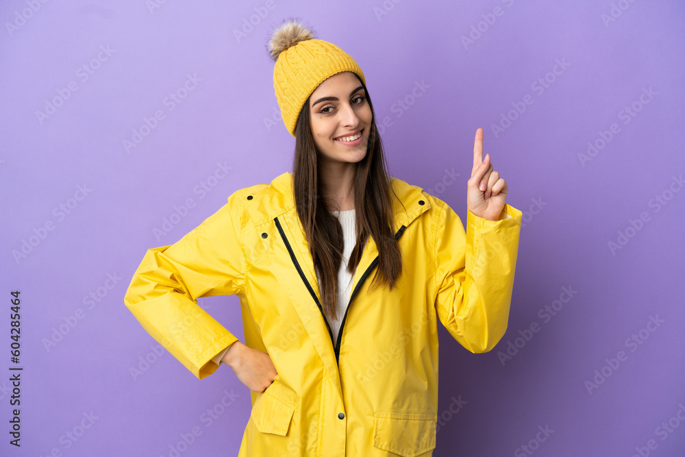 Young caucasian woman wearing a rainproof coat isolated on purple background showing and lifting a finger in sign of the best Young caucasian woman wearing a rainproof coat isolated on purple background showing and lifting a finger in sign of the best
