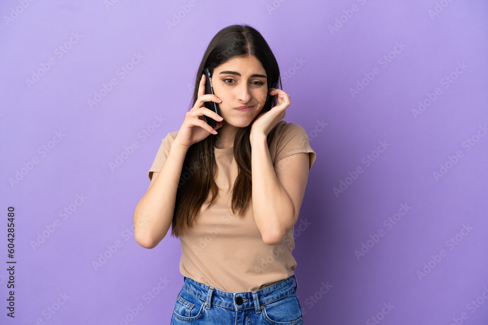 Young caucasian woman using mobile phone isolated on purple background frustrated and covering ears