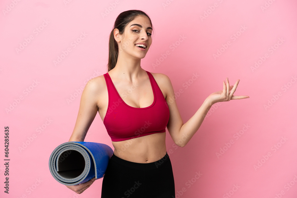Young sport caucasian woman going to yoga classes while holding a mat extending hands to the side for inviting to come Young sport caucasian woman going to yoga classes while holding a mat extending hands to the side for inviting to come