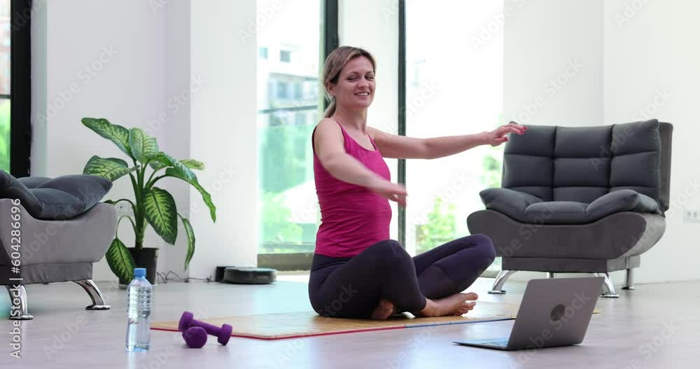 Young fitness trainer, gives video yoga lesson, shows stretching exercises in front of laptop webcam in conference mode. Motivated woman take part in virtual sports training Young fitness trainer, gives video yoga lesson, shows stretching exercises in front of laptop webcam in conference mode. Motivated woman take part in virtual sports training