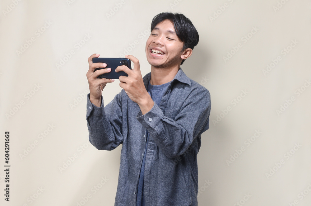 Young Asian man showing surprised facial expression while reading message on his mobile phone Young Asian man showing surprised facial expression while reading message on his mobile phone