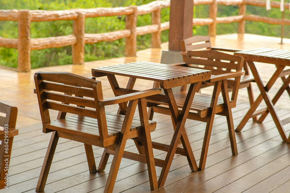 Wooden tables and chairs at outdoor cafe terrace in park. Empty garden furniture surrounded by green garden.