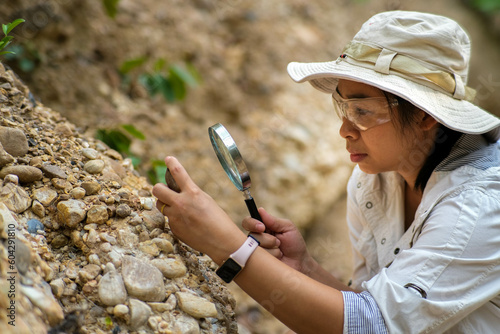 Female geologist using magnifying glass to examine and analyze rock, soil, sand in nature. Archaeologists explore the field. Environmental and ecology research. photo