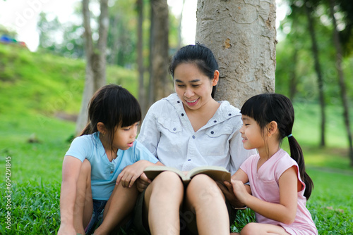 Happy mother and two daughters having fun and enjoying reading at the park. Mother and daughter resting in the summer garden, she reads fairy tales to her daughter.