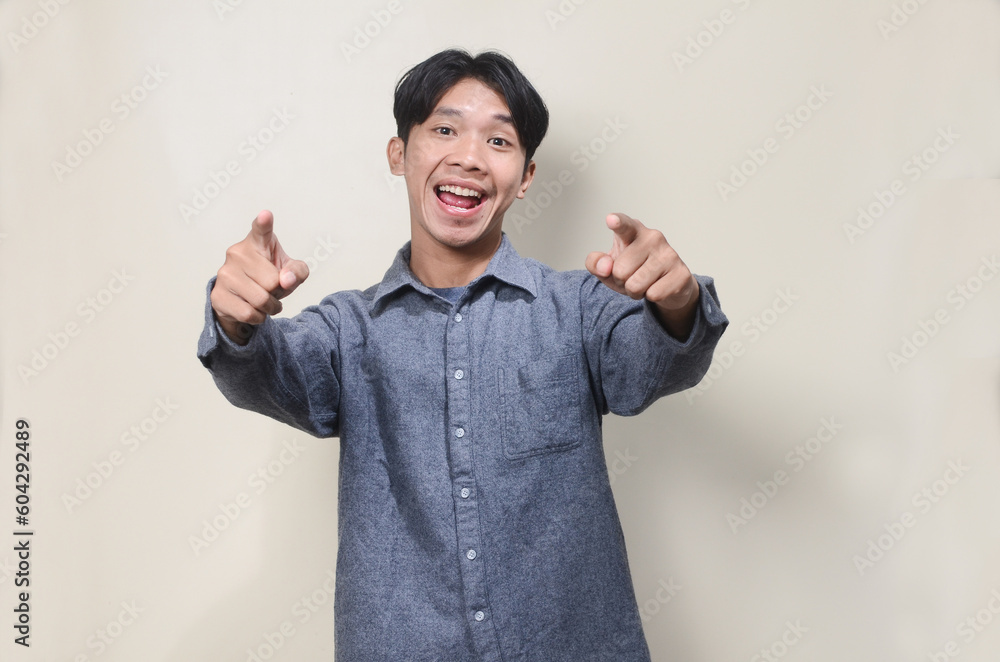Smiling young Asian man wearing gray shirt with hand pointing forward Smiling young Asian man wearing gray shirt with hand pointing forward