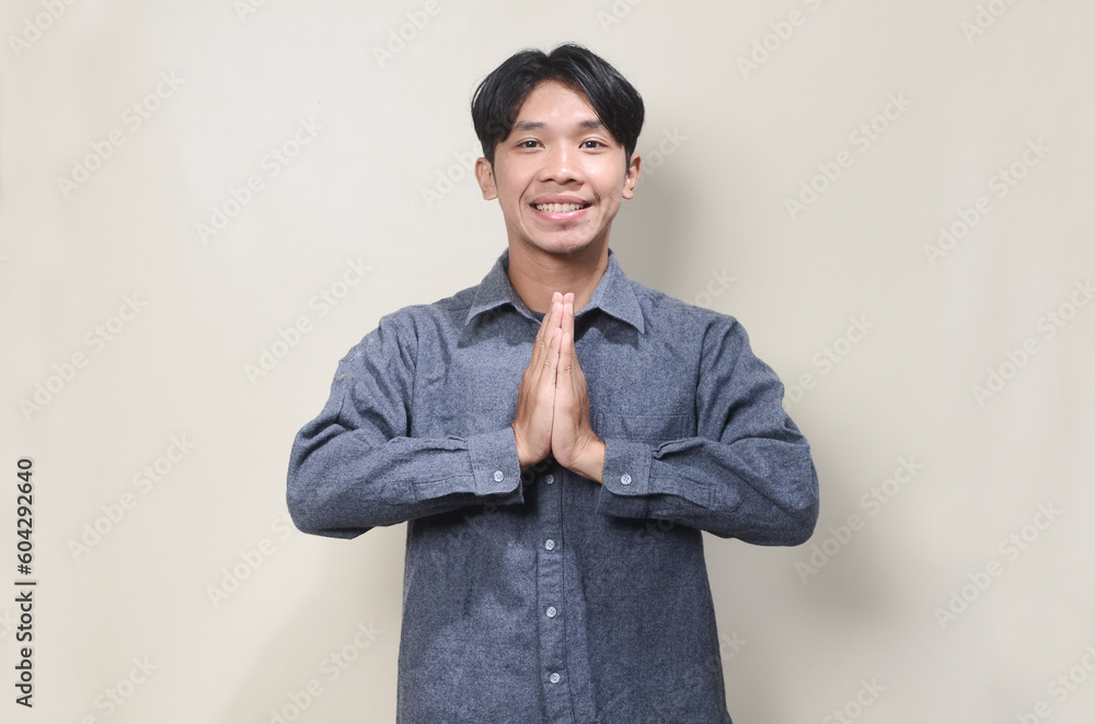 Young Asian man wearing casual shirt with greeting and welcoming gesture Young Asian man wearing casual shirt with greeting and welcoming gesture