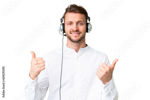 Telemarketer caucasian man working with a headset over isolated chroma key background with thumbs up gesture and smiling © luismolinero