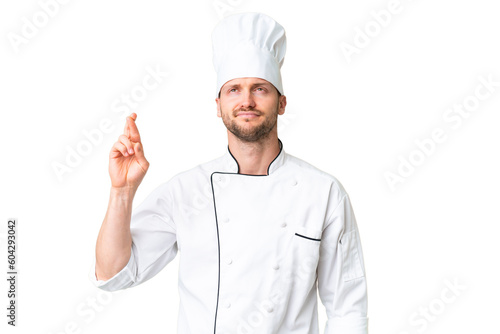 Young caucasian chef over isolated chroma key background with fingers crossing and wishing the best