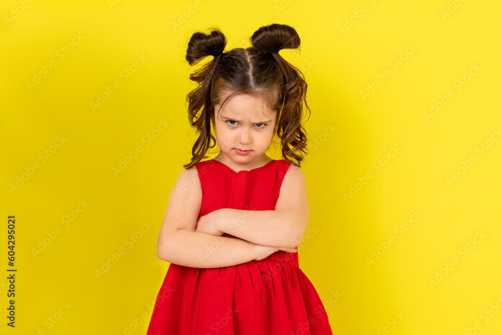 The little girl was offended. a child in a beautiful red dress pouted her lower lip. Yellow background. Vertical. The little girl was offended. a child in a beautiful red dress pouted her lower lip. Yellow background. Vertical.