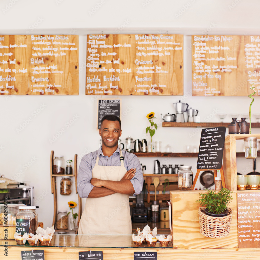 Fototapeta premium Portrait, black man and waiter with arms crossed in cafe with pride for career or job. Barista, smile and confidence of African person from Nigeria as restaurant owner, small business and coffee shop