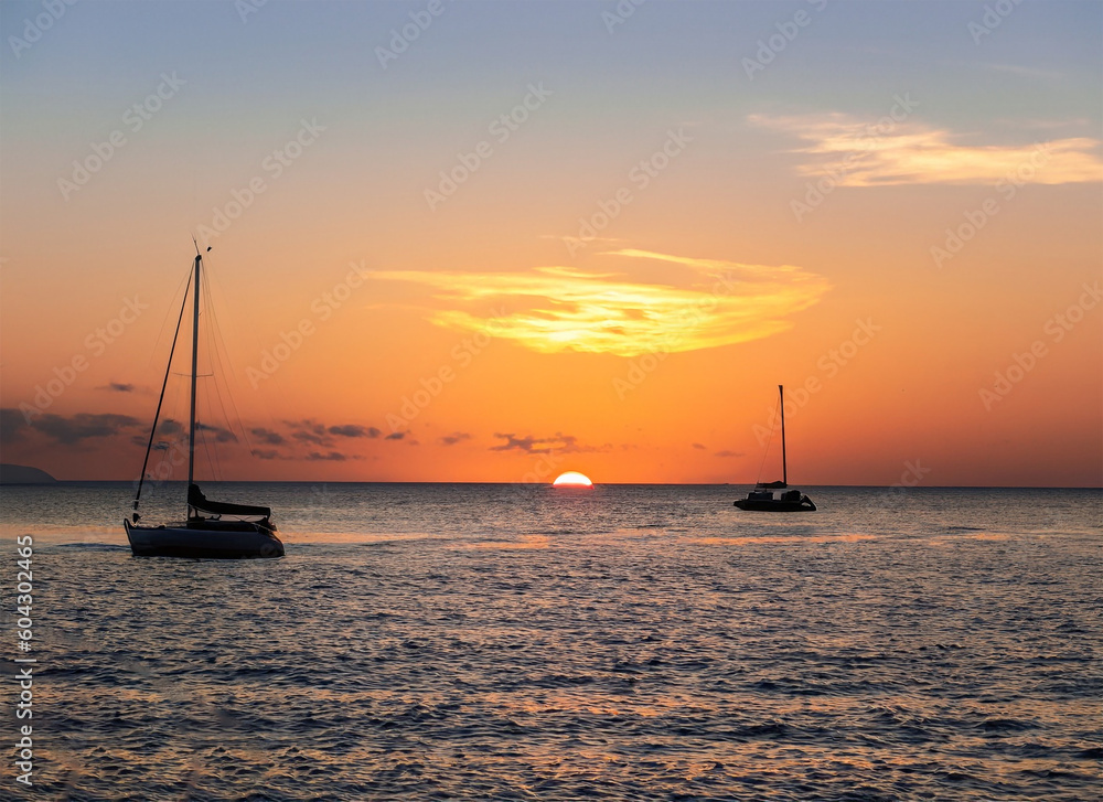 Sunset over the sea with sailboats in the foreground and orange sky. Generated AI