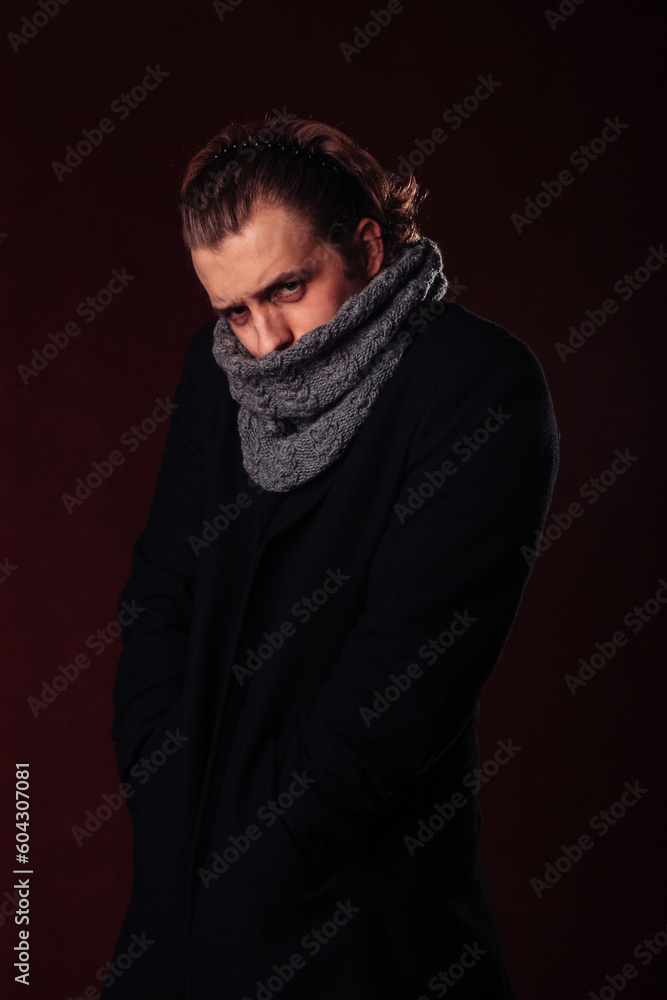 a young man stands pensive and serious in a coat and a knitted scarf