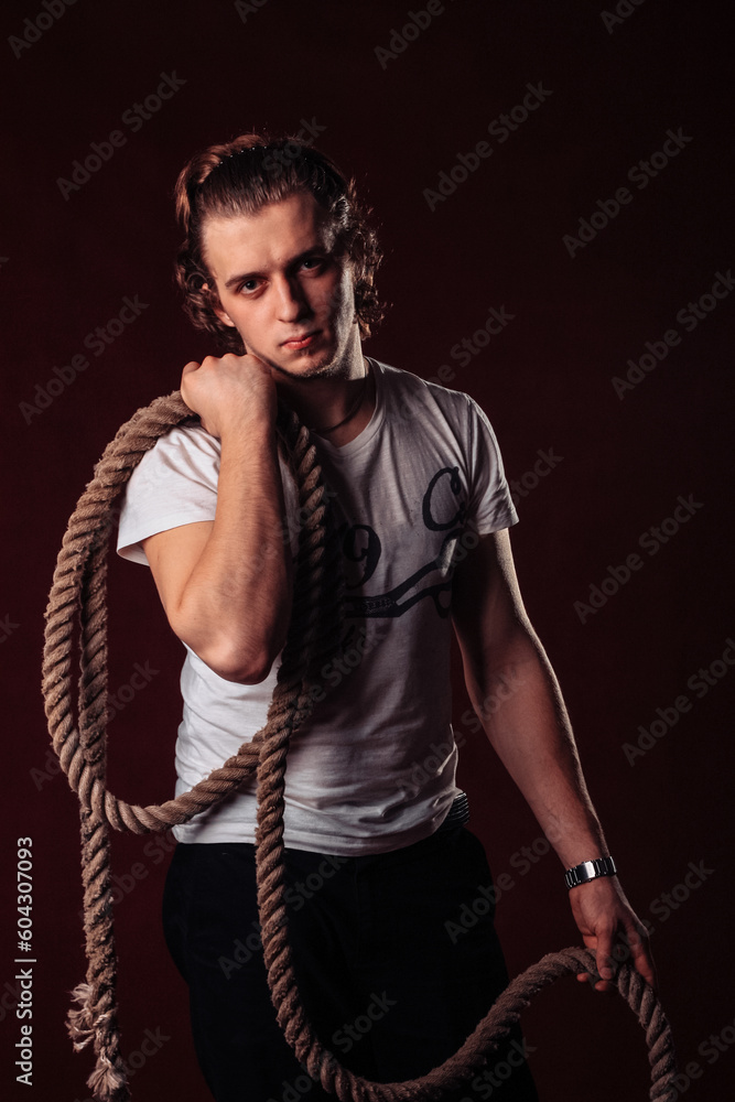 a young man stands with a thick rope in his hands