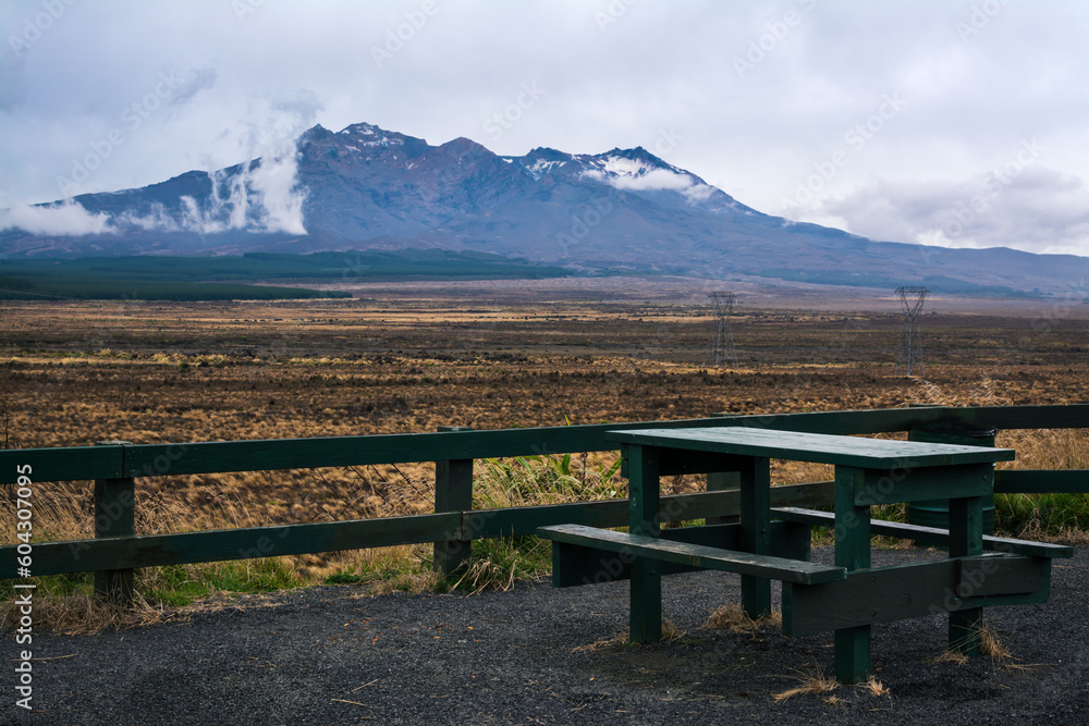 A picnic table witha view over magnificent Mount Ruapehu partially obscured by low clouds. Desolated high land field in Central Plateau of New Zealand. Desert Road, North Island, New Zealand