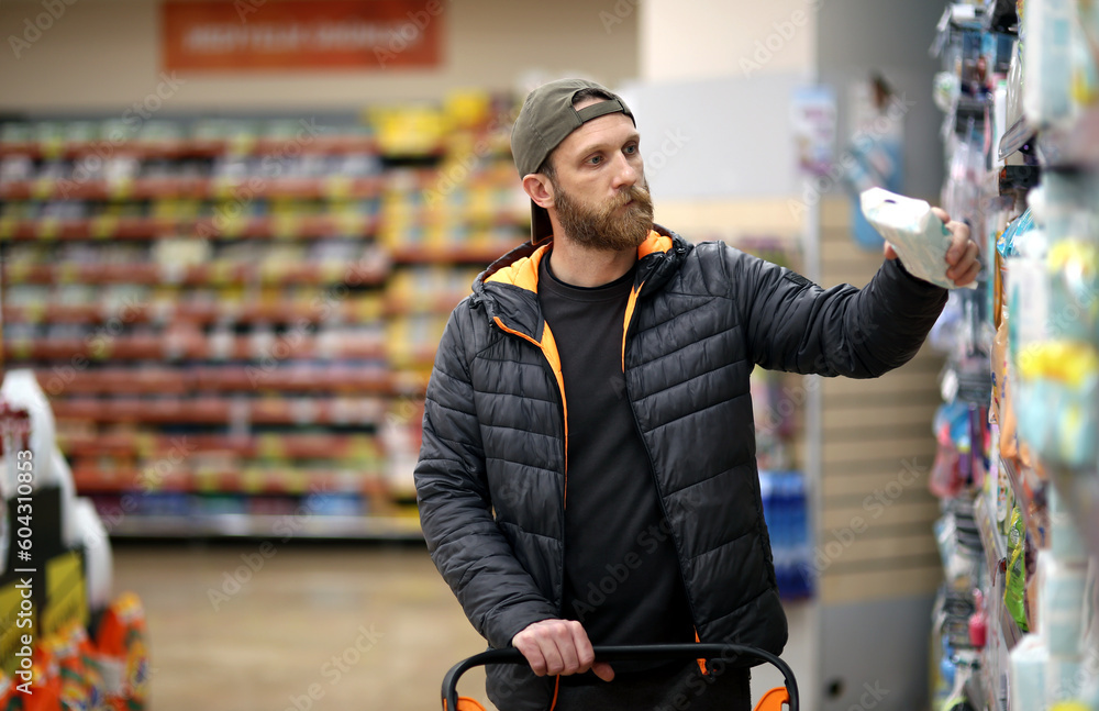 A bearded Caucasian man customer is interested in hygiene products at the supermarket - obrazy, fototapety, plakaty 