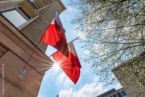 Flag of Poland on facade of a building waving in the wind with sun rays. Celebrating Polish National Flag Day