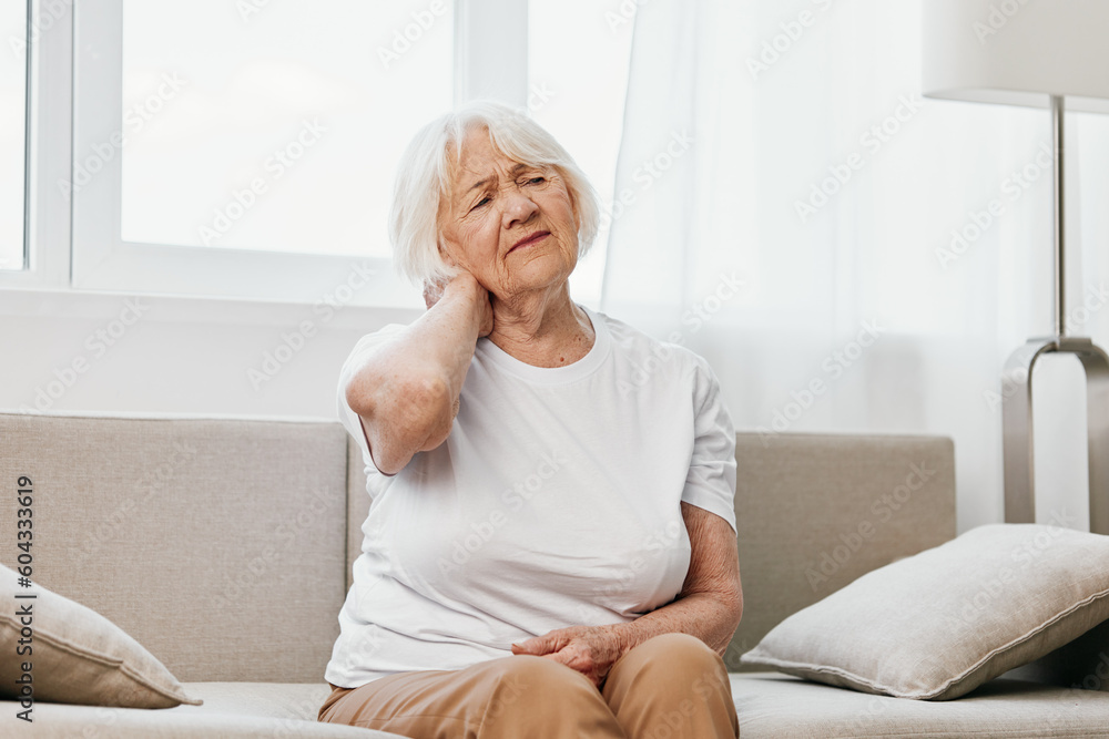 Elderly woman severe neck pain sitting on the sofa, health problems in old age, poor quality of life.