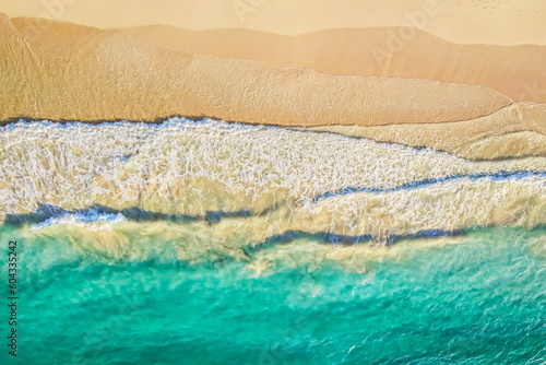 Aerial view of turquoise ocean wave reaching the coastline. Beautiful sand beach from top view. Summer holiday vacation concept. Aerial drone shot of turquoise sea water at the beach, panoramic view.