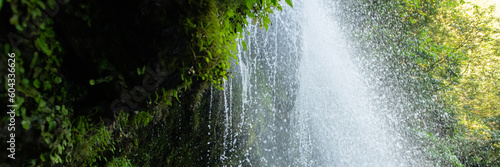 waterfall cascading down rocky cliffs by lush greenery banner