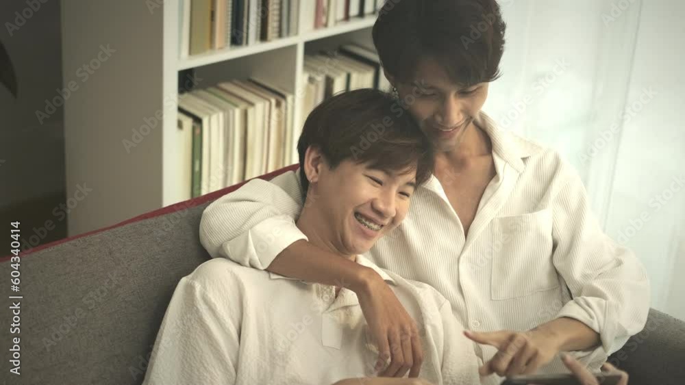 Passionate young gay couple sitting on couch and browsing internet on digital tablet. LGBT, love and lifestyle concept Passionate young gay couple sitting on couch and browsing internet on digital tablet. LGBT, love and lifestyle concept