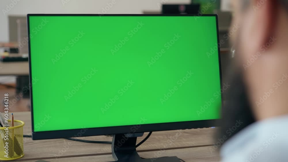 Over the Shoulder: Bearded Middle Aged Man Sitting at His Desk in Office Uses Desktop Computer with Green Mock-up Screen. Close up Green Screen Mock Up Display Over the Shoulder: Bearded Middle Aged Man Sitting at His Desk in Office Uses Desktop Computer with Green Mock-up Screen. Close up Green Screen Mock Up Display