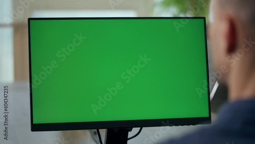 Over the Shoulder: Young Man Sitting at His Desk in Office Uses Desktop Computer with Green Mock-up Screen. Close up Green Screen Mock Up Display