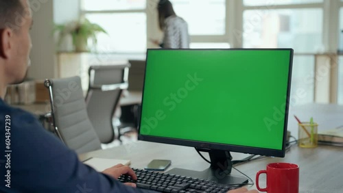 Over the Shoulder: Young Man Sitting at His Desk Uses Desktop Computer with Green Mock-up Screen.Professional Office Employee Working on Computer