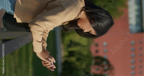 Young teenage Latina college student using social networks with her smartphone in a park, vertical shot