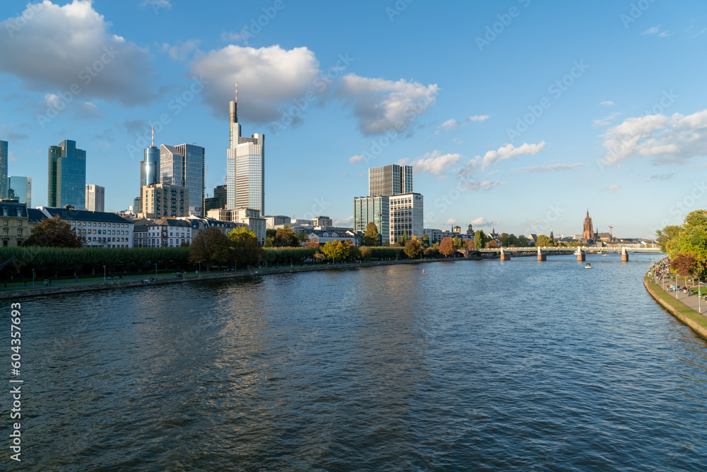 Stunning  of Frankfurt's skyline, featuring its iconic skyscrapers, traffic on the bridge, and a bustling promenade on a partly cloudy day.