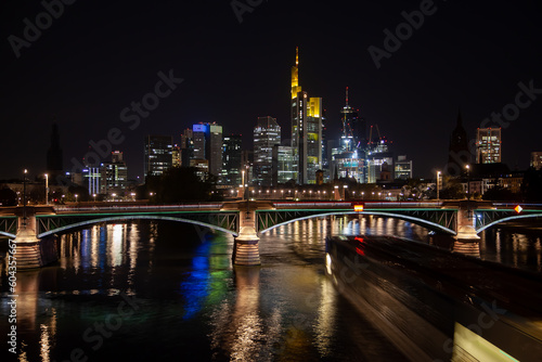 Captivating  of Frankfurt's business district skyline, a bridge illuminated by traffic, and the river with the city's reflection at night. © Yan
