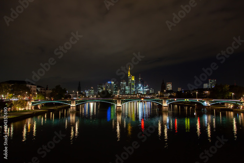 Cityscape  in Frankfurt, Germany featuring a bridge, river, nighttime city illumination reflection, and a downtown skyscrapers background. © Yan