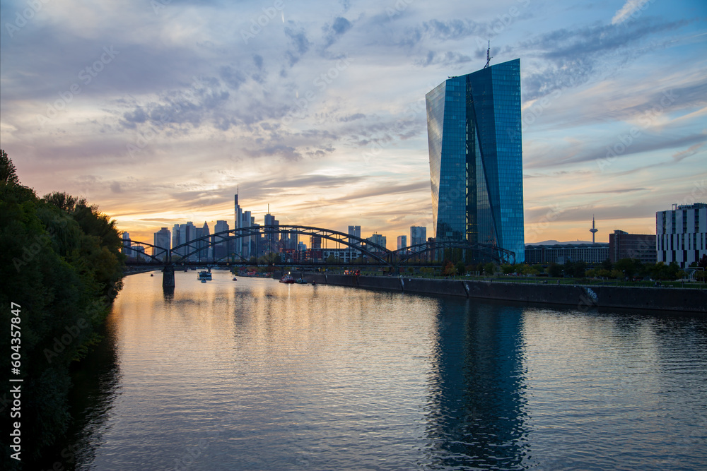 Vibrant sunset  over Frankfurt river, featuring a bridge with traffic, business center skyscrapers, and reflecting illumination.