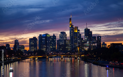 Captivating  of a Frankfurt's skyline at sunset, featuring a bridge, traffic, skyscrapers, and colorful reflections in the river. © Yan