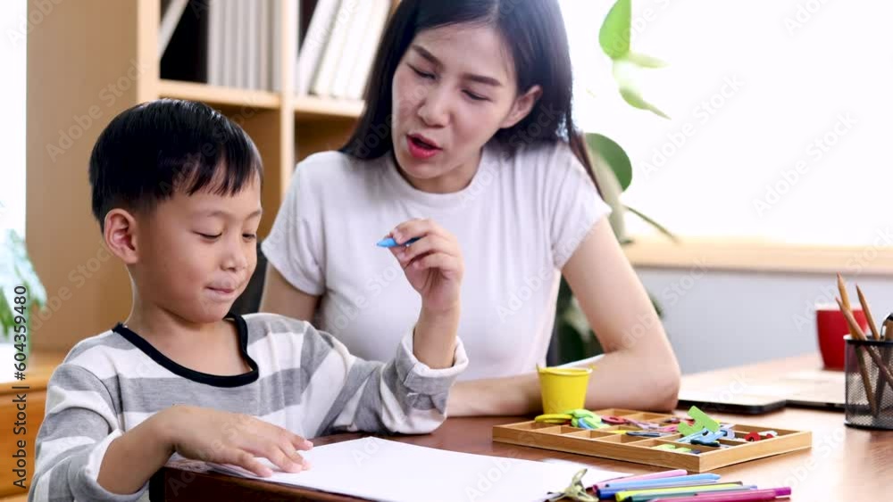 Young beautiful Asian single mother watching her son draw while mother is working from home laptop, adorable boy painting on paper with color pens. Happy family spend time together on holidays. Young beautiful Asian single mother watching her son draw while mother is working from home laptop, adorable boy painting on paper with color pens. Happy family spend time together on holidays.