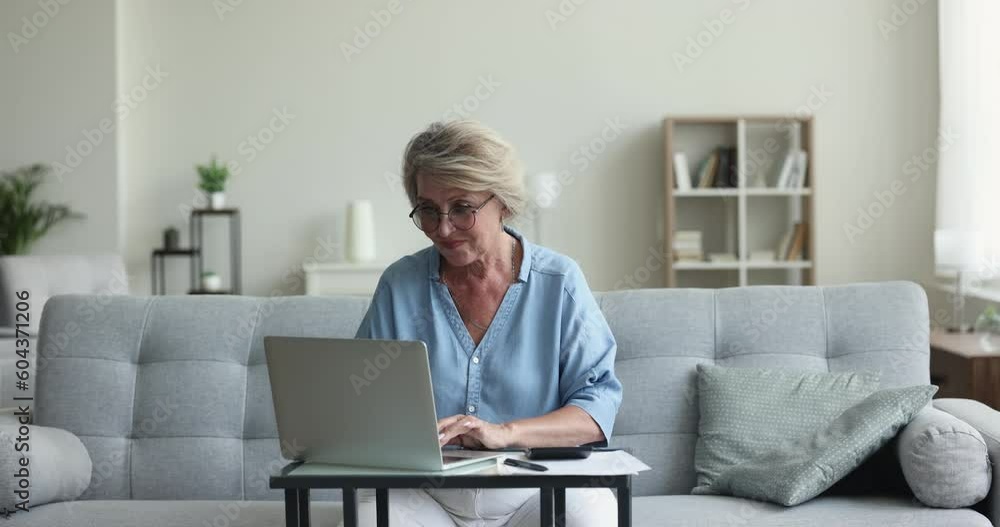 Positive senior homeowner woman typing on calculator and laptop at home, counting budget, savings, expenses, paying taxes, insurance fees, using online financial application for domestic accounting Positive senior homeowner woman typing on calculator and laptop at home, counting budget, savings, expenses, paying taxes, insurance fees, using online financial application for domestic accounting