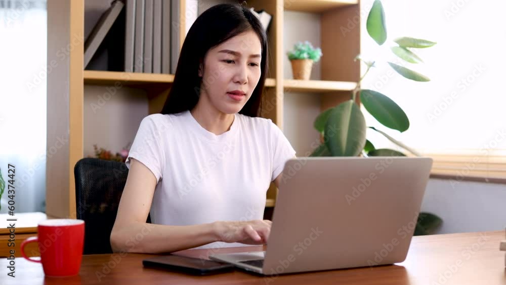Young beautiful asian woman talking with friend on mobile phone while she is working on laptop at home on vacation. Female shopping online choose clothes and dress on social media. Young beautiful asian woman talking with friend on mobile phone while she is working on laptop at home on vacation. Female shopping online choose clothes and dress on social media.
