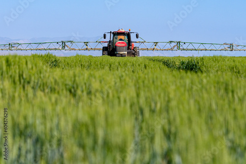 Tractor spray fertilizer on green field. Farming tractor plowing and spraying on field.