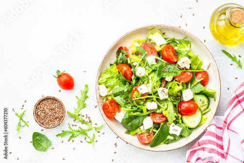 Green salad with spinach, arugula, tomatoes and feta with olive oil. Top view on white.